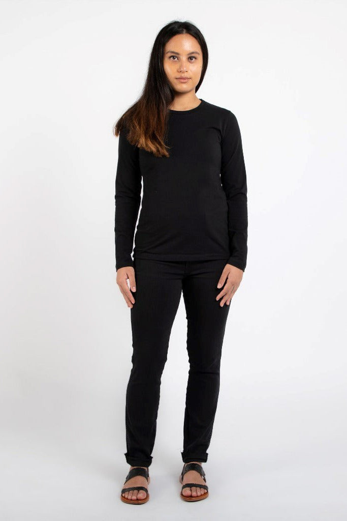 woman with long dyed hair wearing black long sleeve t-shirt and black jeans and sandals against a white backdrop