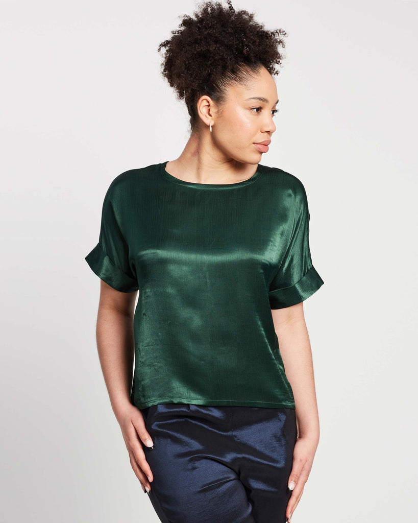 woman wearing scoop neck top in green with rolled sleeve and navy pants