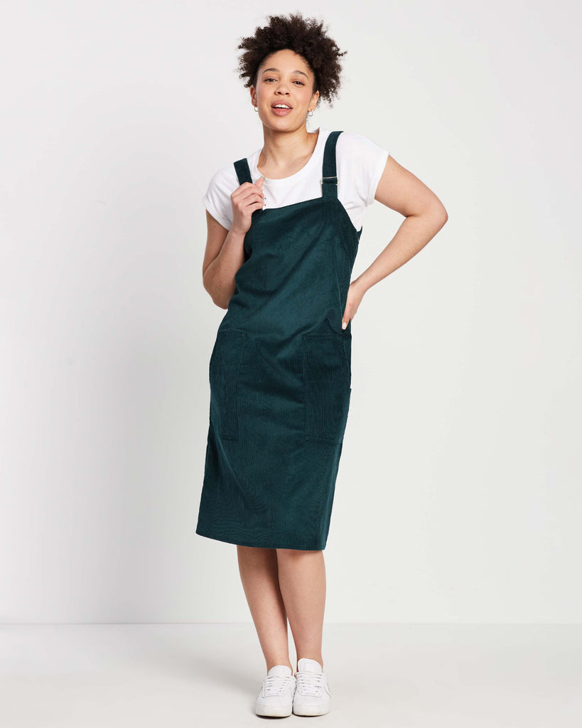 green corduroy pinafore with metal buckles on top of white rolled sleeve t-shirt and white sneakers