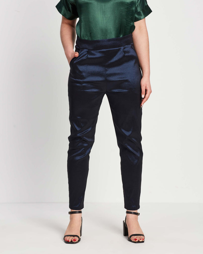 woman wearing navy straight leg pants in shimmery material with green top tucked into pants and black heels