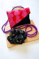 gift set on wooden panel against white backdrop with friendship beads print foldover purse, beaded silk long necklace and scrunchie