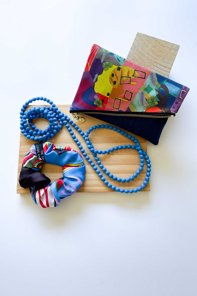 gift set on wooden panel against white backdrop with heirloom print foldover purse, beaded silk long necklace and scrunchie