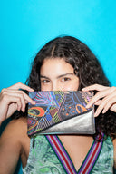 woman with curly hair holding up a colourful purse wearing a green dress against a blue backdrop