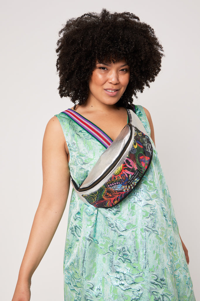 woman with curly hair wearing a cross-body bumbag layered on a green dress against a white backdrop