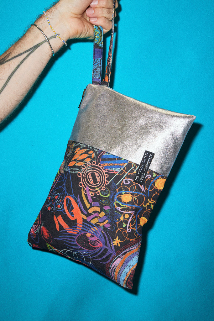 hand holding up a colourful printed clutch by its strap against a blue backdrop