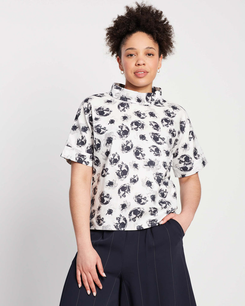 woman wears high rolled neck top with black and white monochrome floral print and cuffed sleeves on top of navy pinstripe wide leg palazzo pants