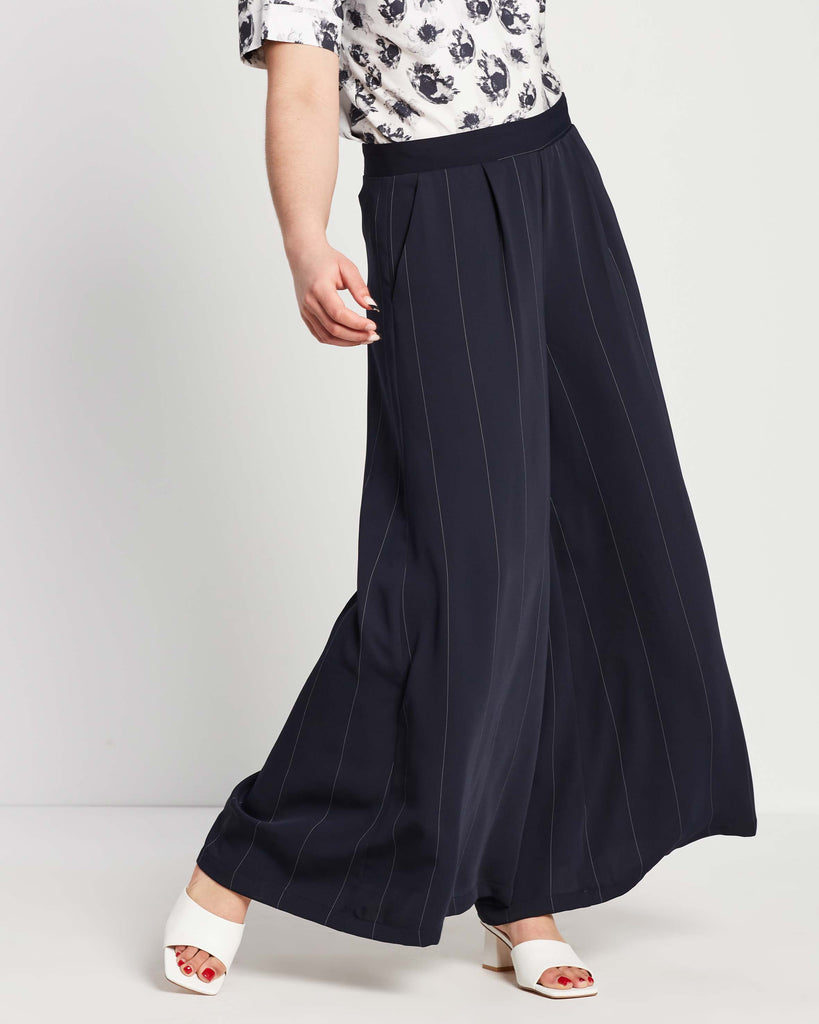woman wearing navy wide leg flowy palazzo pants with pinstripe and floral top tucked into waistband