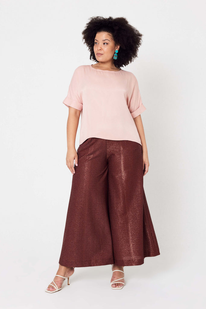 woman with pink scoop top standing with her hands by her side wearing copper pants