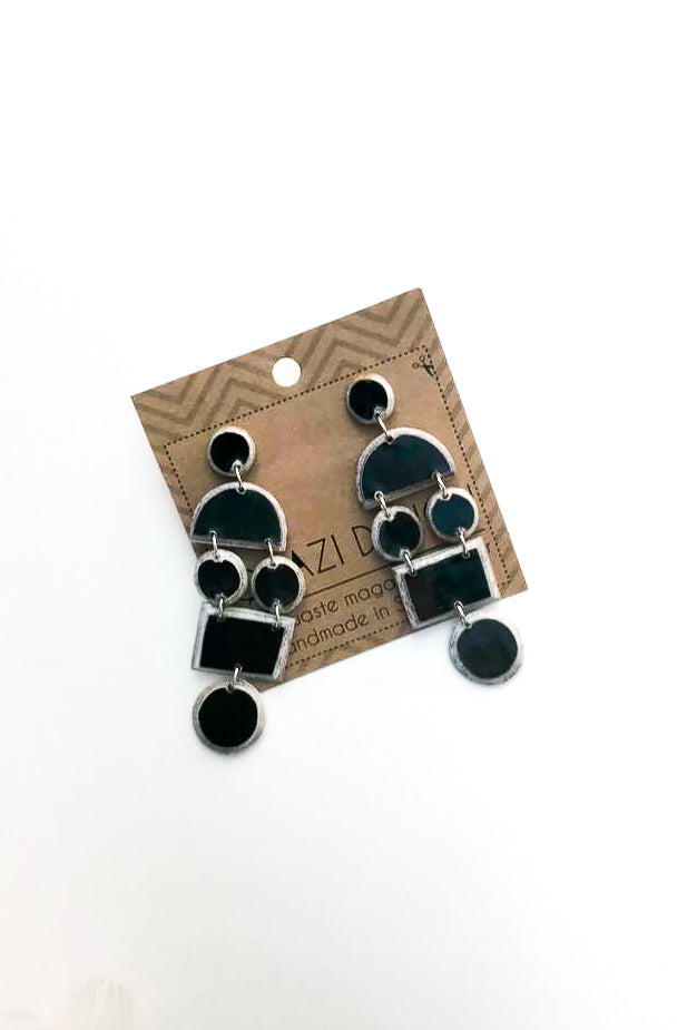 black quazi design earrings on cardboard against a white backdrop