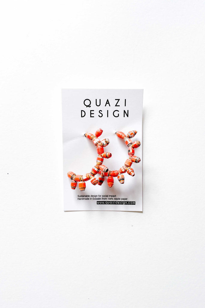 pair of quazi design orange sun earrings against white cardboard on white backdrop